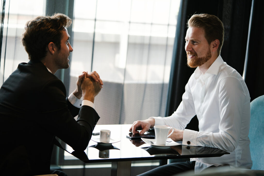 Image of young businessman with cup of coffee communicating with colleague